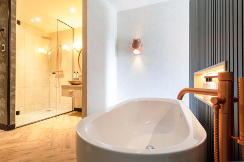 a large white tub in a bathroom with a shower at Boutique Hotel Helder I Kloeg Collection in Renesse