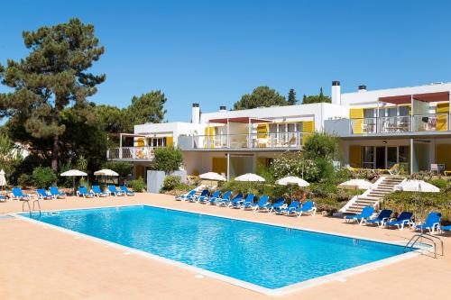 a hotel with a swimming pool with chairs and umbrellas at Apartamentos Turisticos Pinhal Da Marina in Vilamoura