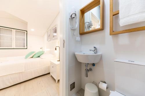 a white bathroom with a sink and a bed at Vila Farol in Nazaré