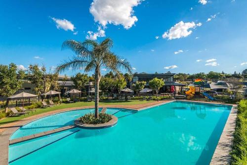una piscina con una palma e un parco giochi di Waterfall Two-Bedroom Apartment a Midrand
