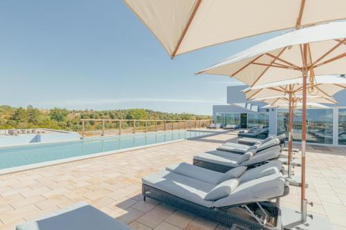 a row of lounge chairs with an umbrella and a pool at Sleep & Nature Hotel in Lavre