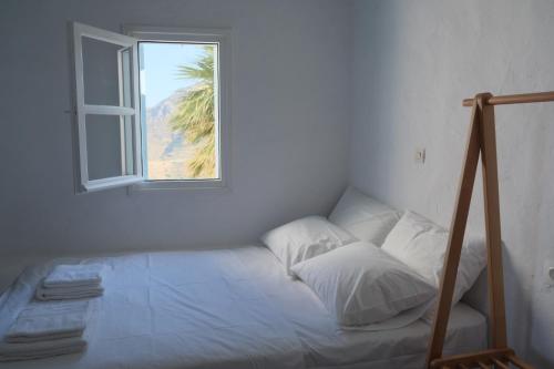 Cama en habitación blanca con ventana en Salty Edge Holiday Home, en Serifos Chora