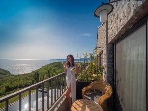 a woman in a white dress standing on a balcony at Vivid Blue Serenity Resort in Sveti Stefan