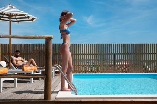 a woman in a bikini standing next to a swimming pool at Lazy Days - Adults Only - Duna Parque Resorts & Hotels in Vila Nova de Milfontes