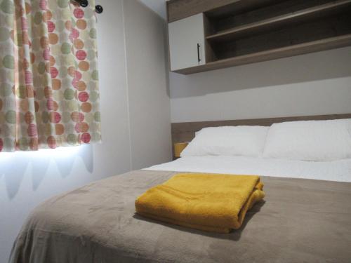 a bedroom with a bed with a yellow blanket on it at Chichester Lakeside Self-Catering Holiday Home in Chichester