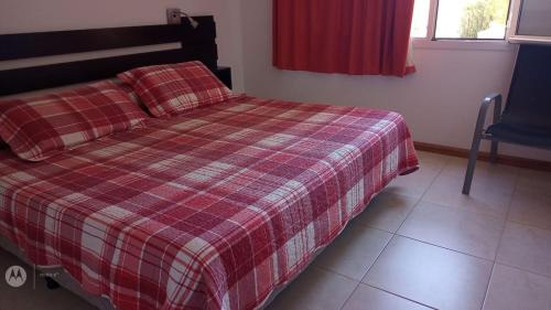 a bedroom with a bed with a plaid blanket and a chair at Coral de Madryn in Puerto Madryn