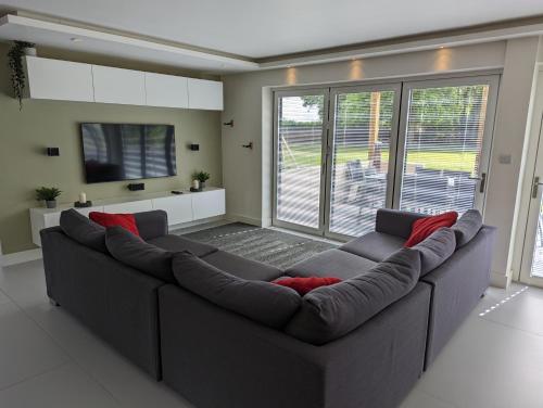 a living room with a large gray couch with red pillows at Unique, Spacious, Self-Built Eco Home with huge garden and movie room in Andover