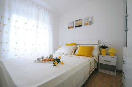 a white bedroom with a large white bed with yellow pillows at Guesthouse Adriana Cottages in Labin