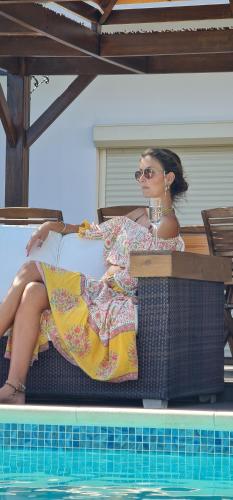 a woman in a dress sitting next to a swimming pool at Villa del Mar in Mazotos