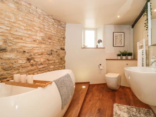 baño con pared de piedra, bañera y lavamanos en Holloway House en Wotton under Edge