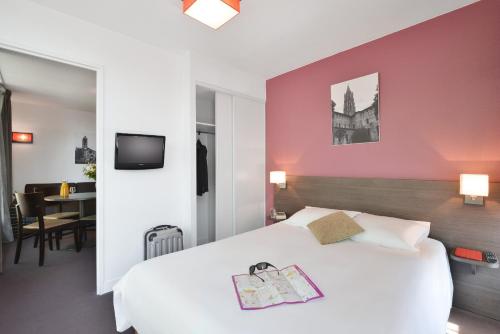- une chambre avec un lit blanc et un mur rose dans l'établissement Aparthotel Adagio Access Toulouse St Cyprien, à Toulouse