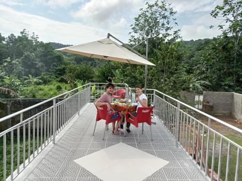 dos personas sentadas en una mesa en un puente con un paraguas en Residencial Brigada, en Santo António