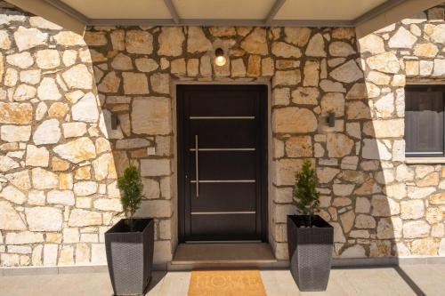 a black door in a stone wall with two plants at Casa Serenity in Agios Ioannis