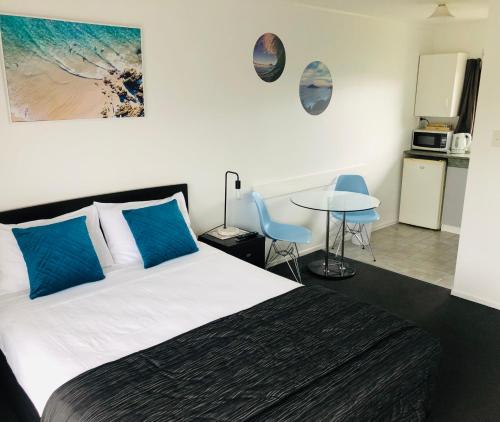 a bedroom with a bed with blue pillows and a table at Blue Haven Motel in Mount Maunganui