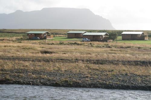 a group of houses in a field next to a body of water at Snorrastadir Accomodation in Kolbeinsstaðir
