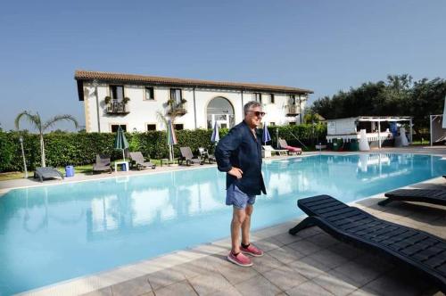 un hombre parado frente a una piscina en Aranceto Hotel Agriturismo en Arenella