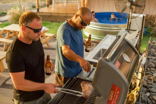 two men cooking food on a grill with bottles of beer at Sky Glamping boutique in Moshav Ramot
