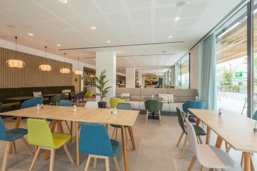 サン・クガ・デル・バリェスにあるHoliday Inn Barcelona - Sant Cugat by IHGの木製テーブルとカラフルな椅子が備わるレストラン