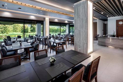 a dining room with tables and chairs and windows at Alpine Golf Resort Chiang Mai in Ban Huai Sai Nua