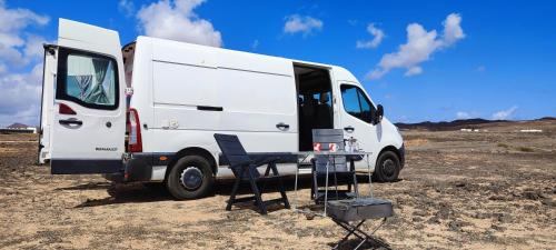 a white van parked in a field with a chair at Se alquila magnifica Camper in Costa Teguise