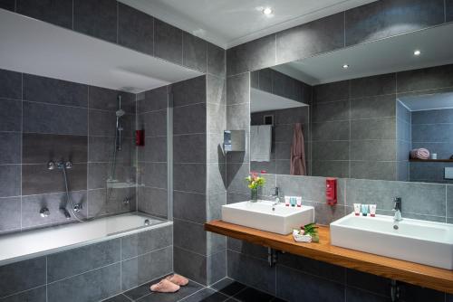 a bathroom with two sinks and a bath tub at Leonardo Royal Hotel Mannheim in Mannheim