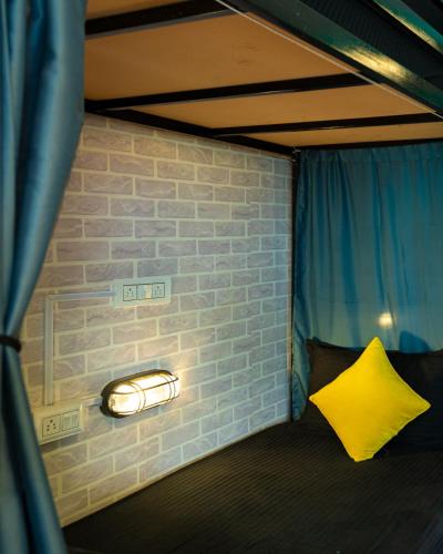 a bed with a yellow pillow and a brick wall at Whoopers Hostel Manali in Manāli