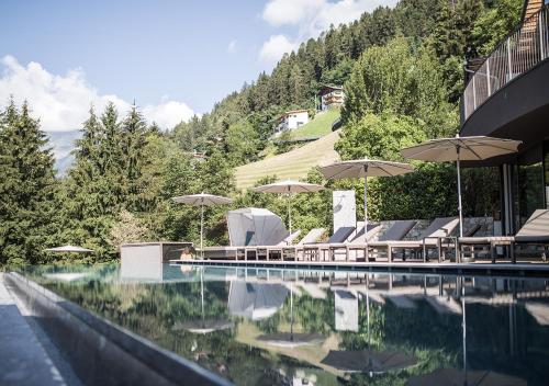 a pool with chairs and umbrellas next to a building at Hotel Bad Fallenbach in San Leonardo in Passiria