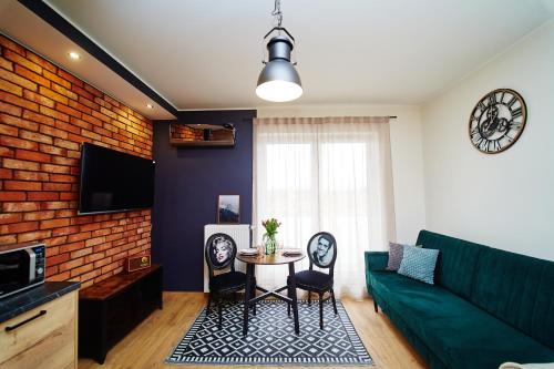 a living room with a green couch and a table at Apartament ,, COŚ NIECOŚ ,, Suwałki LOFT " Wypożycz Rent a PlayStation 5 " KLIMATYZACJA,GARAŻ, ŁADOWANIE AUT ELEKTRYCZNYCH, MONITOROWANE ZAMKNIĘTE OSIEDLE in Suwałki