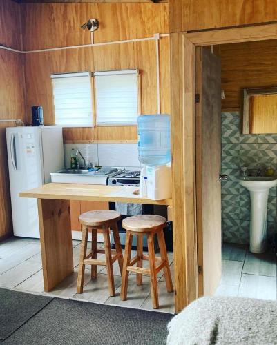 a kitchen with a counter and two stools in it at AUSVIA cabañas tinajas y spa in Hornopiren