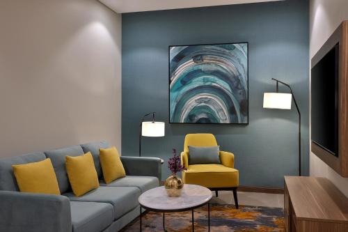 a living room with a blue couch and yellow chairs at Staybridge Suites - Al Khobar City by IHG in Al Khobar