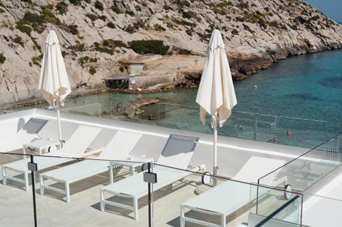 two white umbrellas and a table and chairs next to the water at Hoposa Niu in Cala de Sant Vicent