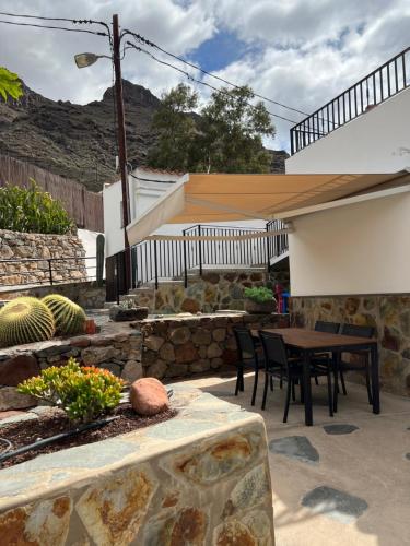 a patio with a table and chairs and a stone wall at Casa rural con baño adaptado y piscina en Mogán in Mogán
