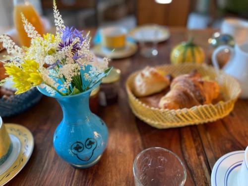 una mesa con un jarrón azul con flores y una cesta de pan en La Corne de Cerf, Forêt de Brocéliande, en Paimpont