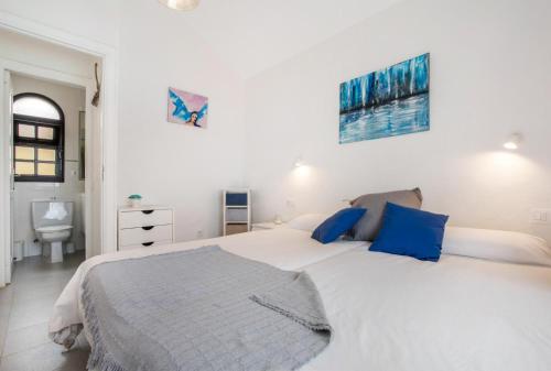a white bedroom with a large bed with blue pillows at Apartamento Vista Piscina o Terraza, Wifi GRATIS in Costa Calma