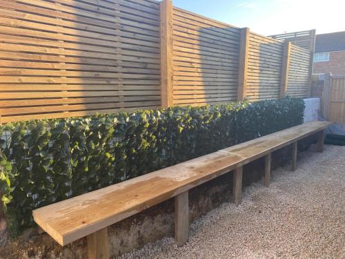 a wooden bench in front of a hedge at Beach, hills, food, scenic walks-The Kelp house. in Peacehaven