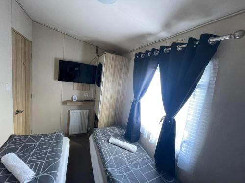 a bedroom with a bed and a window with blue curtains at Holiday Park Caravan Fluffy in Harts Holiday Park in Leysdown-on-Sea