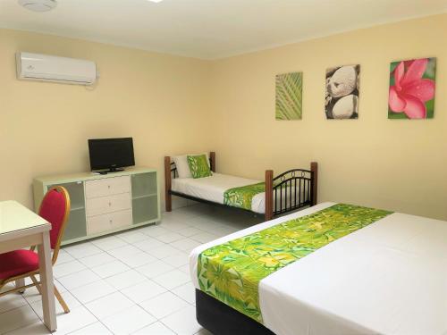 a bedroom with two beds and a desk and a tv at Club Raro Resort- Adults Only in Rarotonga