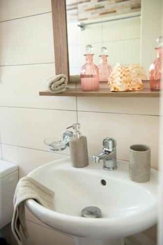 a bathroom sink with a mirror and pink jars at Alexandras On The Beach and Pool apt in Glyfada