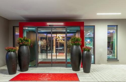 three large metal vases with flowers in front of a building at Leonardo Hotel Augsburg in Augsburg