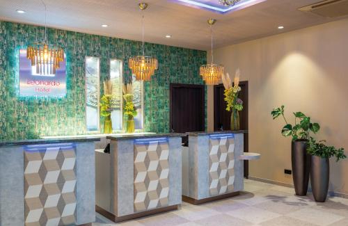 a lobby with a bar with flowers and chandeliers at Leonardo Hotel Augsburg in Augsburg