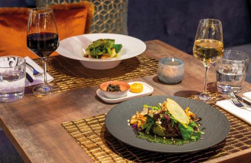 a table with a plate of food and glasses of wine at Leonardo Hotel Augsburg in Augsburg