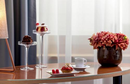 a table with two desserts and a vase with flowers at Leonardo Hotel Zurich Airport in Kloten