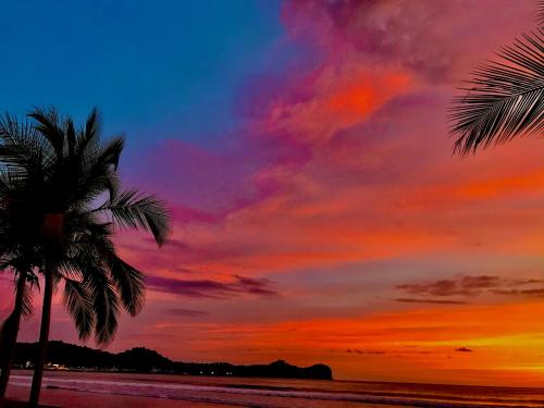 a sunset with two palm trees on the beach at Beachfront Paradise in Manuel Antonio