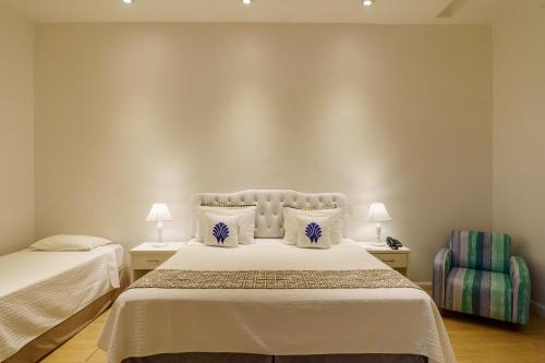 a bedroom with two beds and a chair at Greco Hotel in Búzios