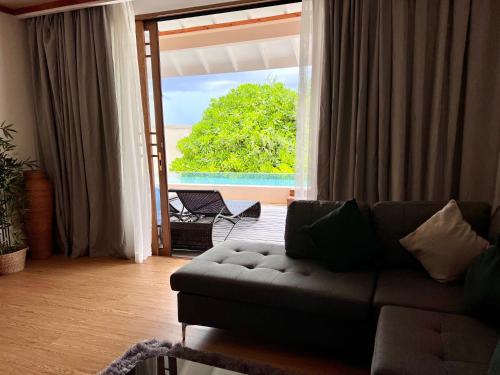 a living room with a couch and a large window at Brennia Kottefaru Maldives in Raa Atoll