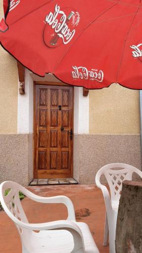 a red umbrella and two white chairs in front of a door at Casa Flor in Arcas