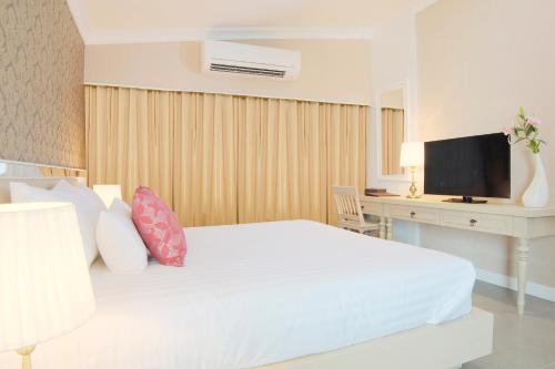 a bedroom with a white bed with a desk and a television at The Raya Surawong Bangkok in Bangkok