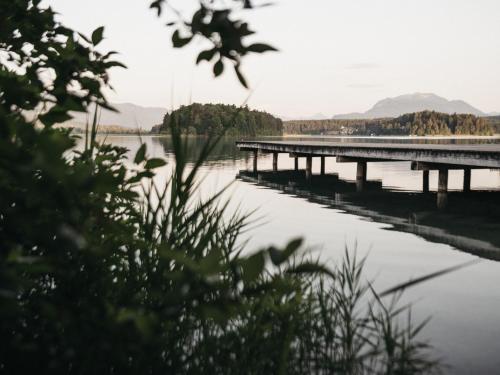 a pier on a lake with mountains in the background at Naturel Hoteldorf Seeleitn in Faak am See