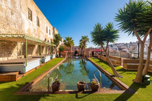 a swimming pool with palm trees next to a building at Vila Origens Boutique Hotel Albufeira – Adults Only in Albufeira