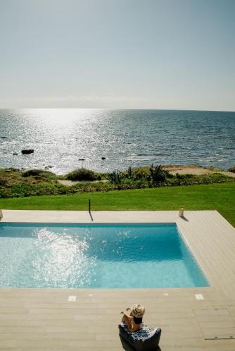 a person sitting in a chair next to a swimming pool at Mirazur Seafront Sunset Villa in Preveza